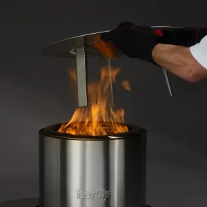 herQs Blaze Heater mit sichtbarer Flamme und erhöhter Metalloberseite, in der Anwendung gezeigt, um die Wärme des herQs Firepit nach unten umzuleiten