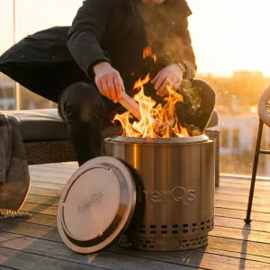 herQs Cozy Closer fire pit lid leaning against a lit metal fire pit on a wooden deck