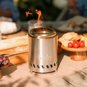 herQs Smokeless FirePit Mini tabletop fire pit burning on a table, with visible flames and brushed steel body.