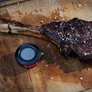 herQs Dome-Thermometer neben einem gegrillten Steak auf einem Holzbrett zum Grillen von Fleisch