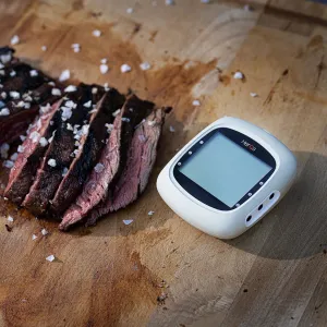 herQs EasyBBQ trådlös termometer med appnotiser bredvid skivat grillat kött på en träbräda
