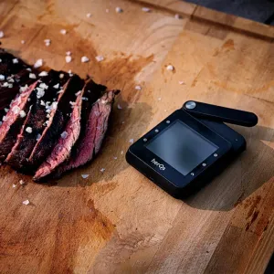 herQs kabelloses Thermometer mit sechs Sonden neben aufgeschnittenem Grillfleisch auf einem Schneidebrett aus Holz