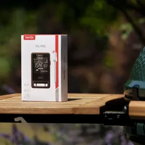 herQs Pin PRO Fleischthermometer-Verkaufsverpackung mit 2 kabellosen Sonden auf einem Gartentisch neben einem Grill