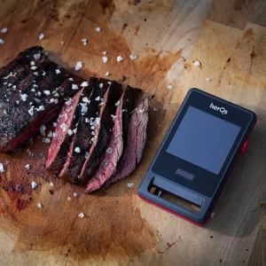 herQs Pin PRO kabelloses Fleischthermometer neben aufgeschnittenem Grillfleisch auf einem Holzbrett