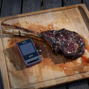 herQs Pin PRO kabelloses Fleischthermometer neben einem gegarten Tomahawk-Steak auf einem Schneidebrett aus Holz