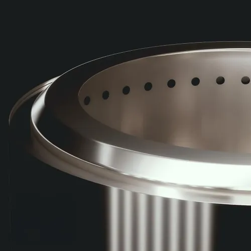 Close-up of round stainless steel fireplace with perforated inner edge of small round holes and vertically grooved polished outer wall.