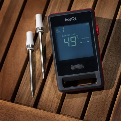 herQs Pin PRO kødtermometer med display, der viser 49 °C, knap og grebsåbning; to metalprober med hvide håndtag på træbord.