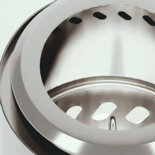 Kiiltävästä ruostumattomasta teräksestä valmistettu takka, lähikuva pyöreästä yläosasta, jossa on tuuletusaukot, ja sisäpuolelta, jossa on soikeat aukot sisäpuolella