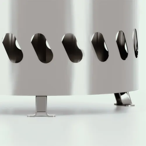 Kompakti lieriömäinen takka ruostumatonta terästä, jossa on alareunan ympärillä soikeat ilmanvaihtoaukot ja joka seisoo pienillä pöytäjaloilla kirkasta pintaa vasten.